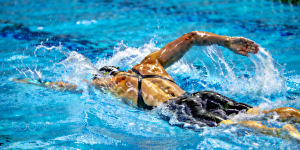 游泳运动员在蓝色泳池中破浪前行，水花四溅